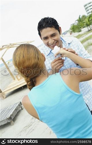 Young woman holding an ice-cream in front of a mid adult man&acute;s mouth