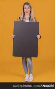 young woman holding blank black placard hand against orange background