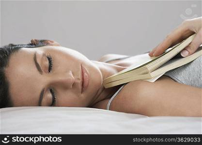 Young woman holding book asleep on bed, close-up