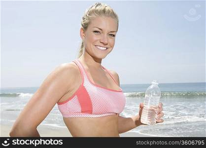 Young woman holding bottle of water at the beach