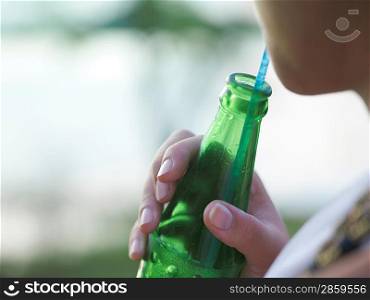 Young woman holding bottle using drinking straw mid section
