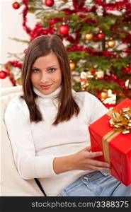 Young woman holding Christmas present in front of tree