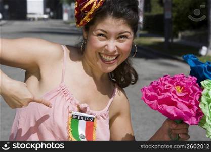 Young woman holding colorful flowers and pointing at Mexican flag
