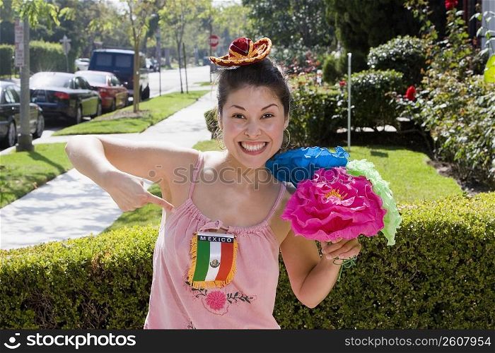Young woman holding colorful flowers and pointing at Mexican flag