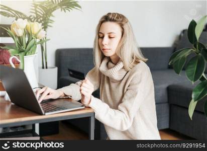 Young woman holding credit card and using laptop.  Woman working at home. Online shopping,  internet banking,  working from home concept