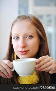 young woman holding cup of coffee and looking out window. She drinks coffee at cafe