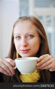 young woman holding cup of coffee and looking out window. She drinks coffee at cafe