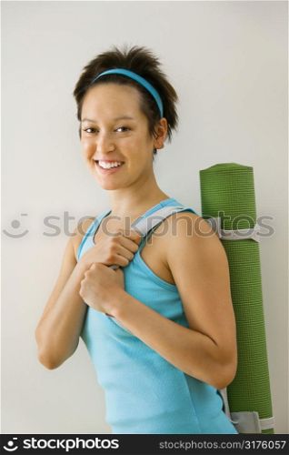 Young woman holding exercise mat and smiling.