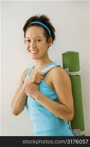 Young woman holding exercise mat and smiling.