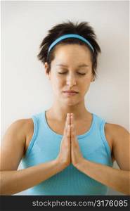 Young woman holding hands in prayer position with eyes closed meditating.