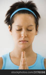 Young woman holding hands in prayer position with eyes closed meditating.