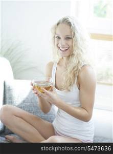 Young woman holding herbal tea cup while sitting on sofa