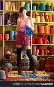 Young Woman Holding Knitting Standing In Front Of Yarn Display