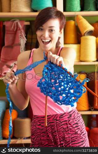 Young Woman Holding Knitting Standing In Front Of Yarn Display