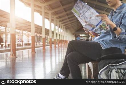 young woman holding map with backpack sitting on platform at train station - travel concept