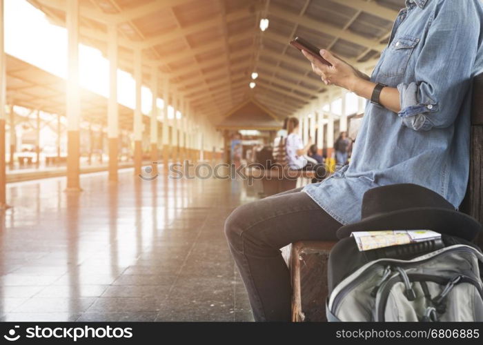 young woman holding map with backpack sitting on platform at train station - travel concept