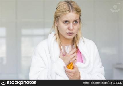Young woman holding medicine and glass of water while suffering from cold