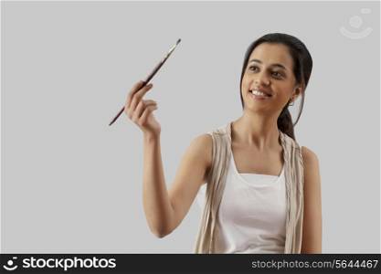 Young woman holding paintbrush isolated over gray background