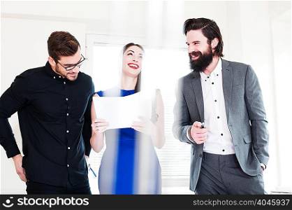 Young woman holding paper laughing with male colleagues
