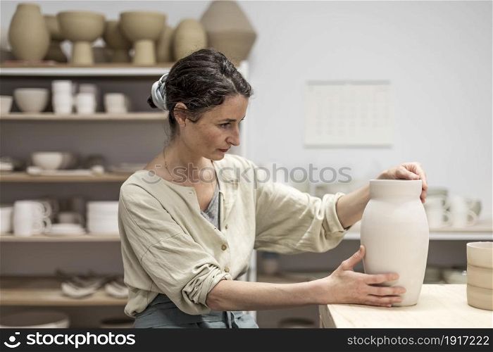 Young woman holding pottery instrument for scraping, smoothing, shaping and sculpting. Lady siting on bench with pottery wheel and making clay pot. Lady siting on bench with pottery wheel and making clay pot