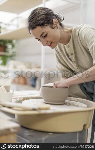 Young woman holding pottery instrument for scraping, smoothing, shaping and sculpting. Lady siting on bench with pottery wheel and making clay pot. Lady siting on bench with pottery wheel and making clay pot