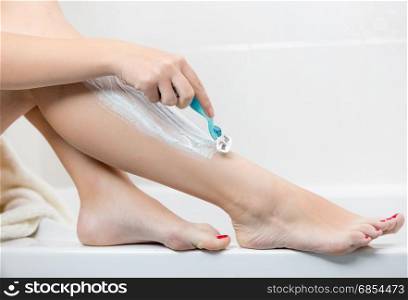 Young woman holding razor and shaving legs at bathroom