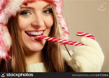 Young woman holding sweet candy cane in mouth. Girls hands wear woolen white gloves. Christmas time concept.