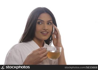 Young woman holding tea cup while using cell phone