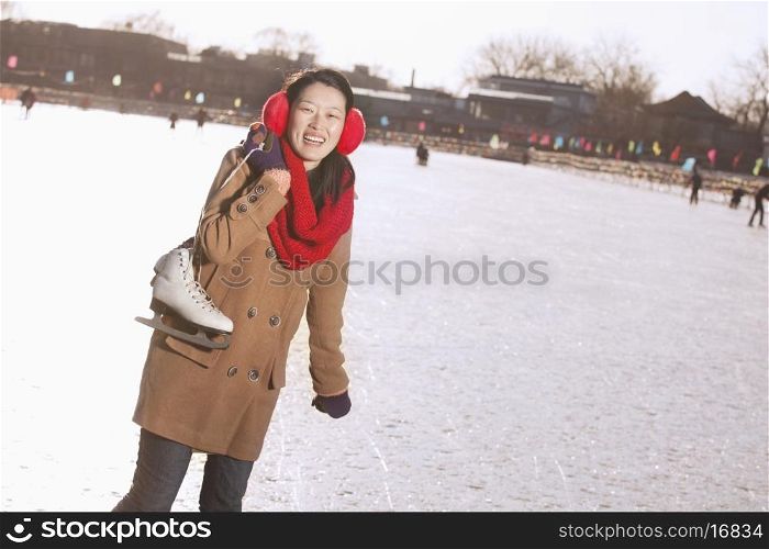 Young Woman Holding Up Ice Skates Outside, Beijing