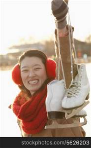 Young Woman Holding Up Ice Skates Outside, Beijing