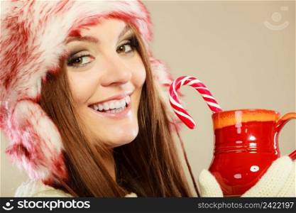 Young woman holding xmas mug with candy cane. Girls hands in woolen white gloves. Christmas time concept.. Girl with cane in xmas mug.