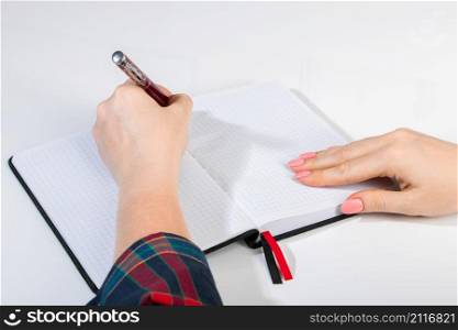 Young woman holds a pen in her left hand and writes a note in blank notebook. International Left-Handers Day. Young woman holds a pen in her left hand and writes note in blank notebook. International Left-Handers Day