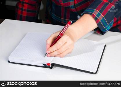 Young woman holds a pen in her left hand and writes a note in blank notebook. International Left-Handers Day. Young woman holds a pen in her left hand and writes  note in blank notebook. International Left-Handers Day