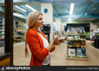Young woman holds glass with fish, pet store. Female person buying equipment in petshop, accessories for domestic animals. Young woman holds glass with fish, pet store