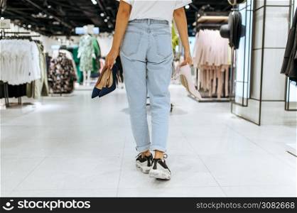 Young woman holds many shoes in clothing store, back view. Female person shopping in fashion boutique, shopaholic, shopper looking on boots. Young woman holds many shoes in clothing store