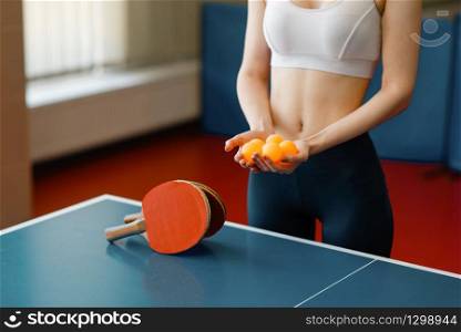 Young woman holds ping pong balls at the game table indoors. Female person in sportswear, training in table-tennis club