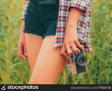 Young woman holds retro style camera in her hand while traveling in outdoor nature landscape in summer.
