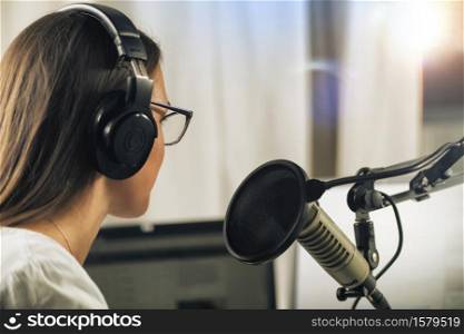 Young Woman Hosting an online talk show from her studio, wearing headphones, talking to the microphone, side view. Young Woman Hosting a Talk Show from Her Studio, Wearing Headphones, Talking to the Microphone