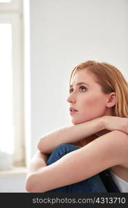 Young woman hugging knees and looking up