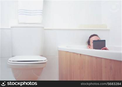 Young woman in a bathtub is reading on a tablet