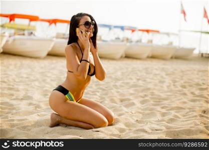 Young woman in a bikini on the beach using a mobile phone