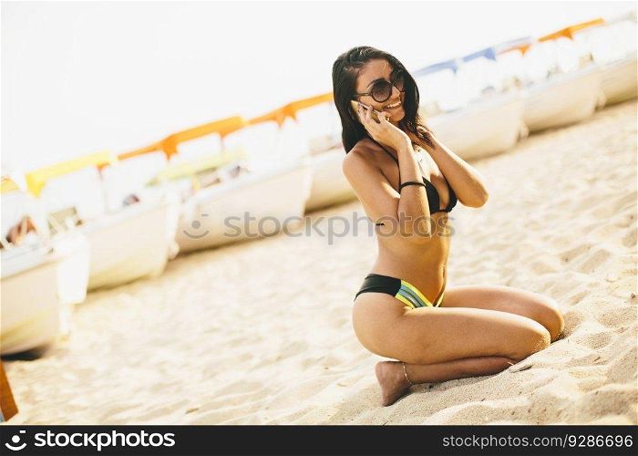 Young woman in a bikini on the beach using a mobile phone