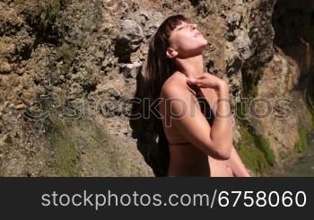 young woman in a bikini washing near the waterfall