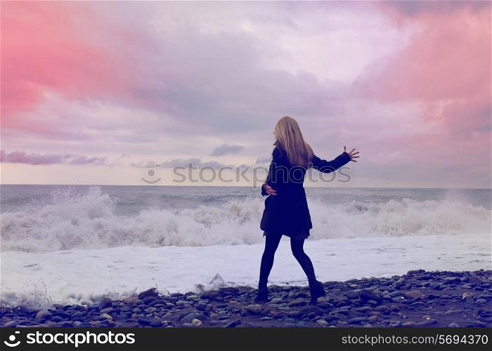 Young woman in a black coat and hat on the beach