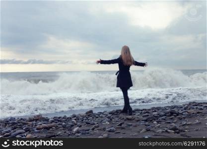 young woman in a black coat on the beach