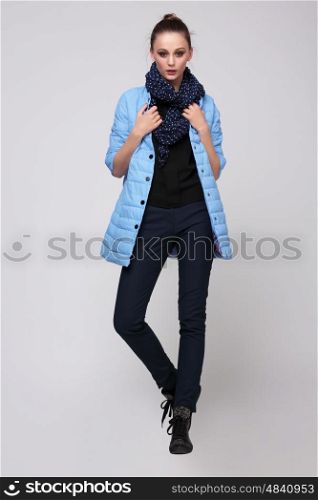 Young woman in a blue jacket with a scarf around his neck and pants, posing in studio full-length. Fashion.