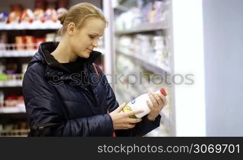 Young woman in a dairy section of supermarket putting a bottle of milk in her shopping basket