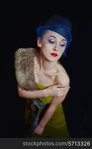 young woman in a green dress and hat veils on black background close up