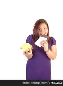 Young woman in a purple dress holding a yellow apple and a chocolatebare, liked the chocolate bar more, for white background.