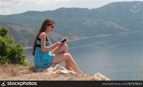 young woman in a short blue dress reading the e-book by the sea